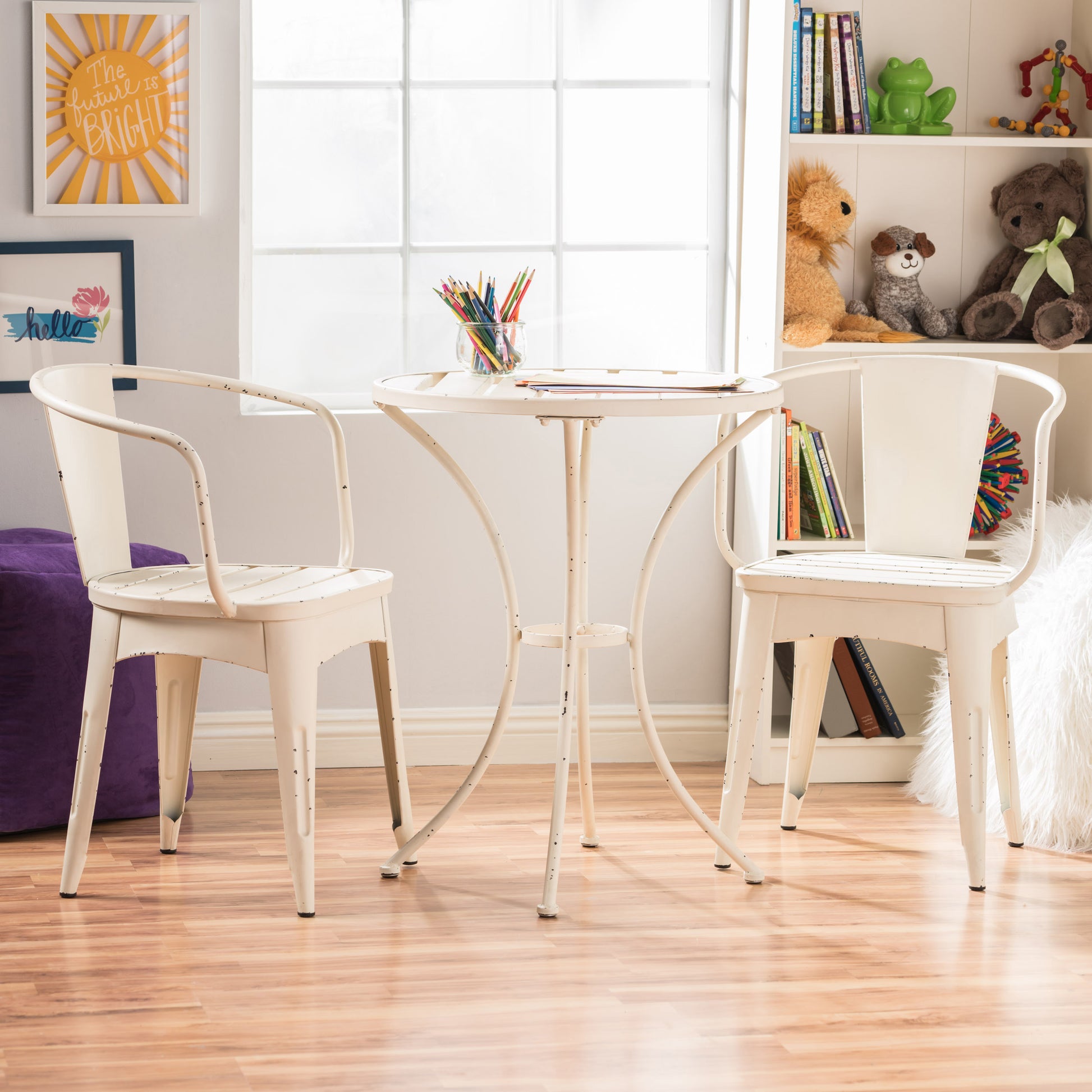 A white 3-piece patio bistro dining set, consisting of two chairs and a round table, is placed on a patio with a study room and greenery in the background.