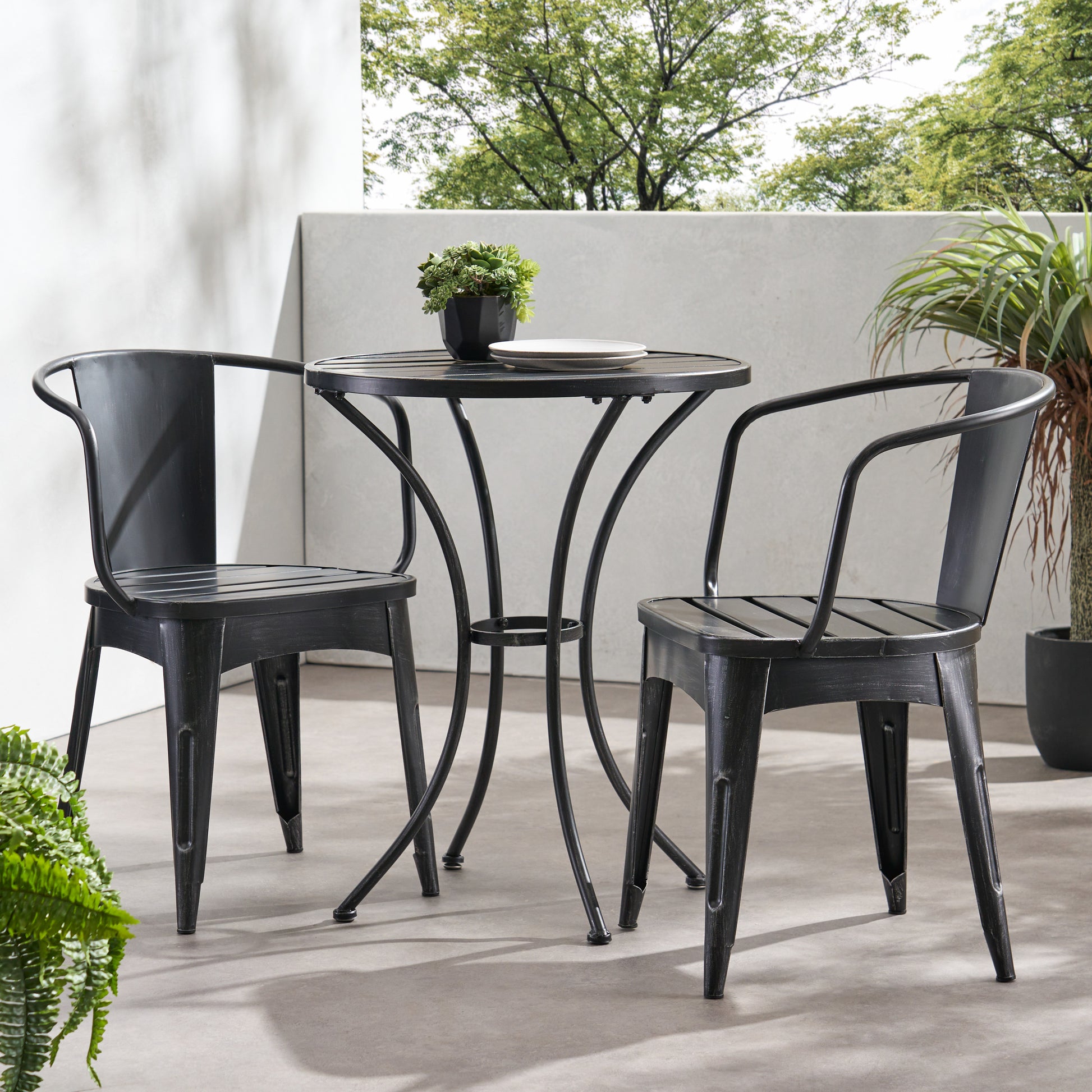 A black 3-piece patio bistro set, consisting of two chairs and a round table, is placed on a patio with a pool and greenery in the background, KOSSMAI
