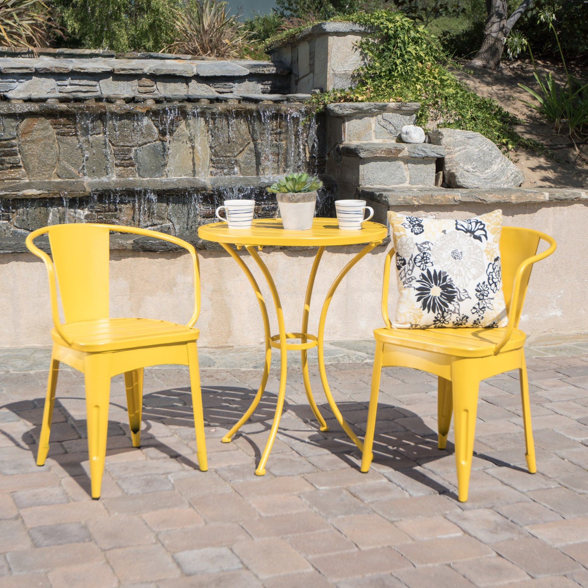 A yellow 3-piece patio bistro dining set, consisting of two chairs and a round table, is placed on a patio with a pool and greenery in the background.KOSSMAI